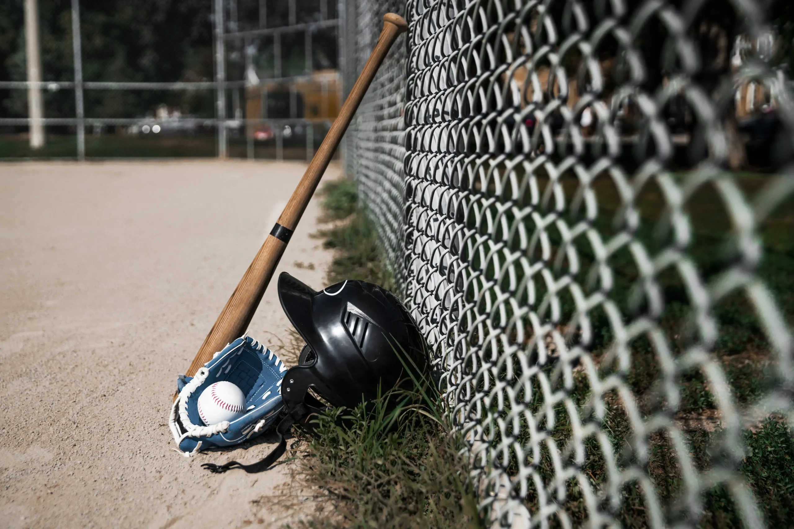 Baseball gear by a fence bat, helmet, glove, and baseball